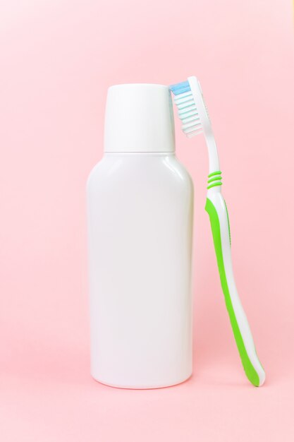 White mouthwash bottle and toothbrush on pastel pink.