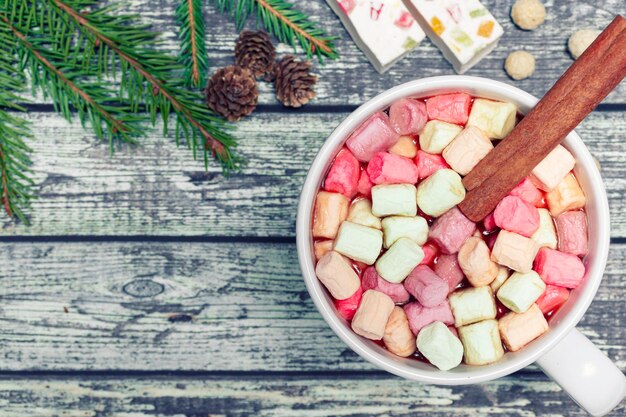 Foto tazza bianca di cioccolata calda fresca con marshmallow e bastoncino di cannella su fondo di legno natale