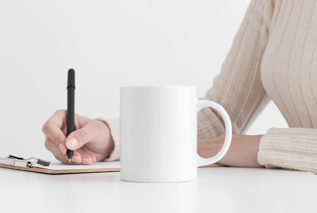 クリップボードにメモを取る女性と白いマグカップのモックアップ