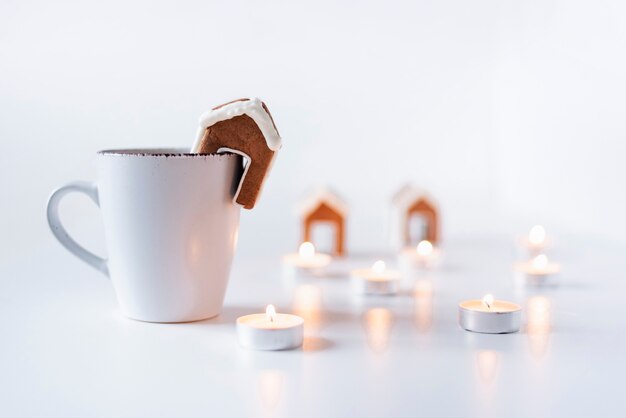 White mug, small gingerbread house and candles. Christmas holidays.