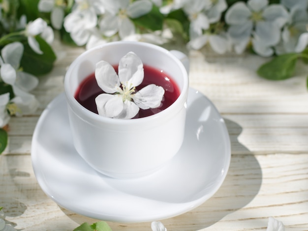 White mug of tea on a wooden table, apple blossoms in the background