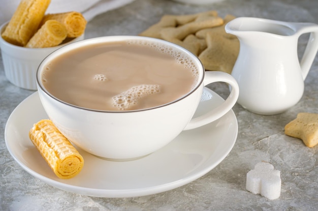 Tazza bianca con una bevanda con latte su un tavolo bianco tra cialde e biscotti