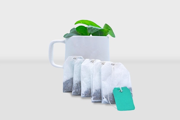 A white mug with green tea bags in front of it with green leaves inside the cup