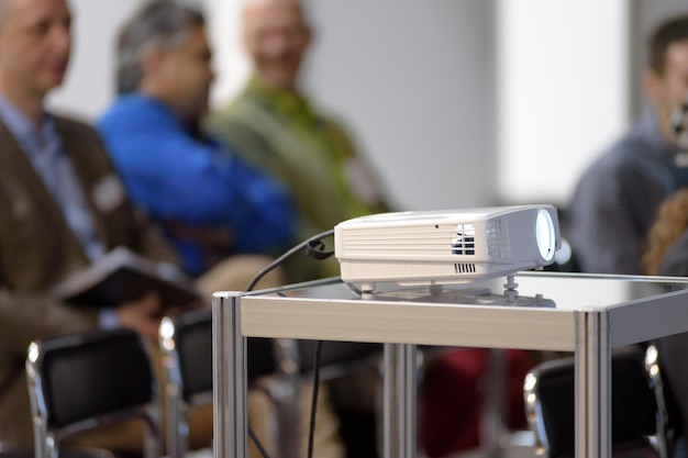 White multimedia projector in a conference room with blured people on the background