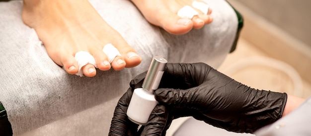 Smalto per unghie bianco nelle mani di un manicure mentre dipinge le unghie su un primo piano di piedi femminili
