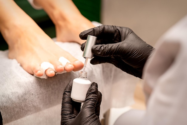 Foto smalto per unghie bianco nelle mani di un manicure mentre dipinge le unghie su un primo piano di piedi femminili