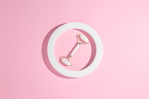 White natural quartz face roller in a round presentation frame on a pink background. Top view, flat lay.