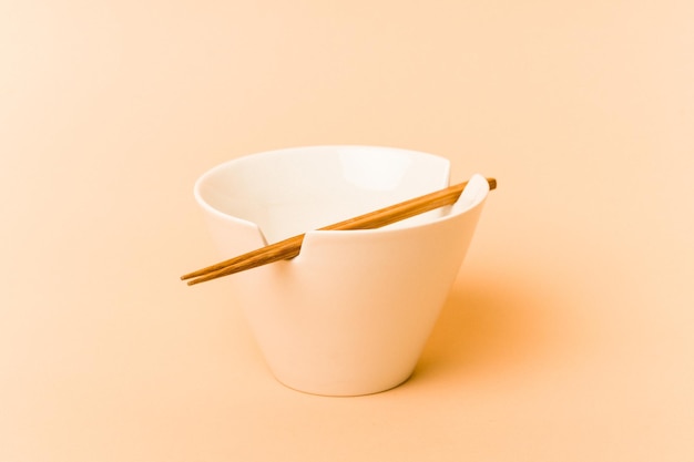 Белая миска с лапшой и палочками для еды на бежевом фоне