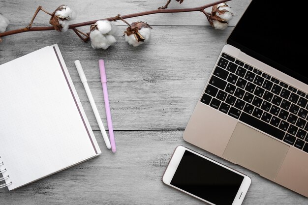 White notebook shot from above on a wooden light table next to a cotton branch, a golden laptop and a phone