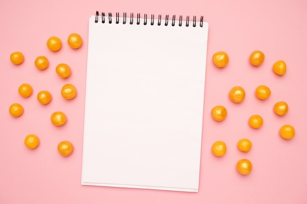 White notebook and sweet yellow candies on a pink 
