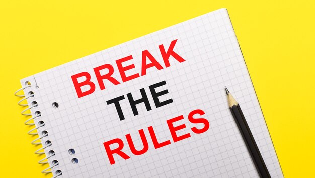 Белый блокнот с надписью BREAK THE RULES, написанной черным карандашом на желтом фоне.