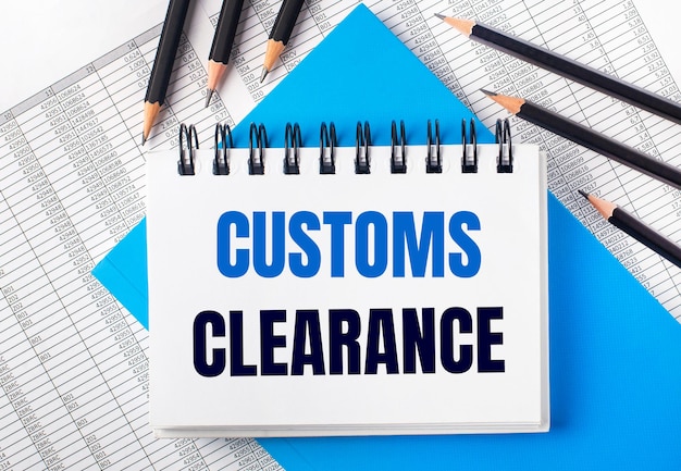 파란색 배경에 검정 연필 옆에 있는 테이블에 CUSTOMS CLEARANCE라는 텍스트가 있는 흰색 노트북 및 보고서. 비즈니스 개념