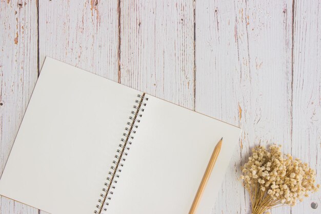 White notebook with wooden pencil and white flowers on wooden table