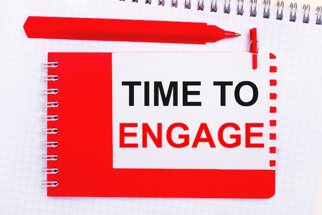 On a white notepad, a red pen, a red notepad and a white sheet of paper with the text TIME TO ENGAGE