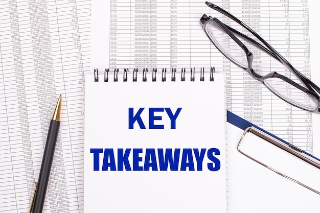 Белый блокнот с текстом KEY TAKEAWAYS, ручка и очки лежат на белом офисном столе Вид сверху