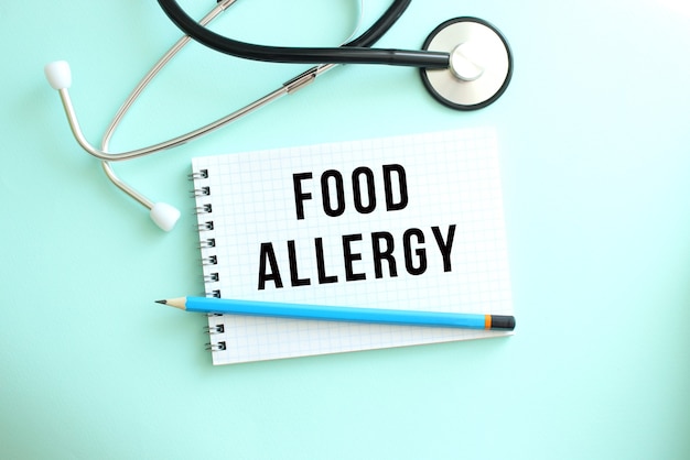 White notepad with the words food allergy and a stethoscope on a blue background