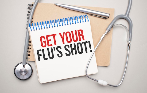 Белый блокнот с надписью «Сделай снимок гриппа» и стетоскопом на синем фоне. Медицинская концепция