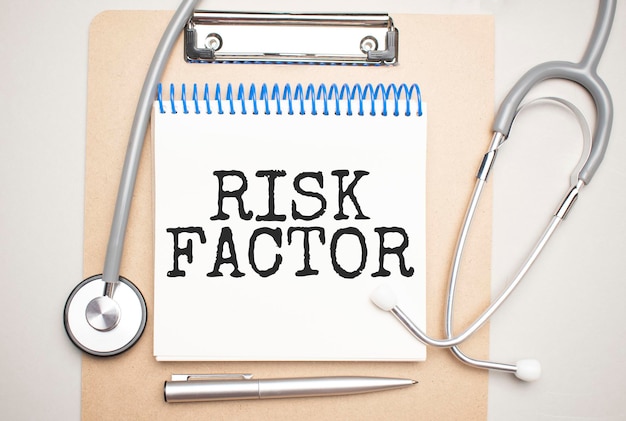 Blocco note bianco con le parole fattore di rischio e uno stetoscopio su sfondo blu. concetto medico
