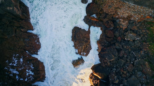 White ocean foam splashing on dark coastal rocks slow motion aerial stormy sea