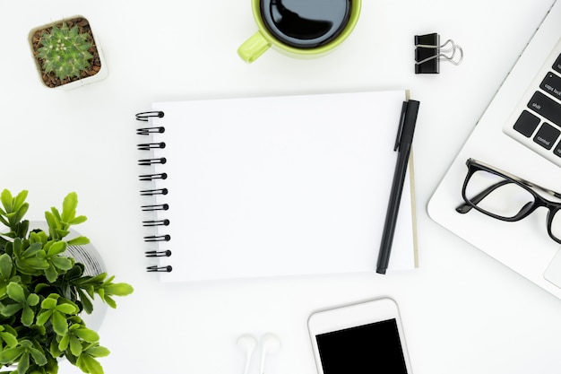 White office desk table with blank notebook page and supplies. 