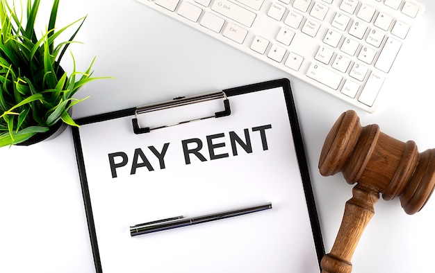 빈 시트, 텍스트 PAY RENT, 키보드 및 망치가있는 흰색 사무실 책상 테이블