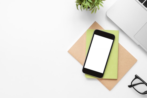 White office desk table with smartphone with blank screen and other office supplies. 