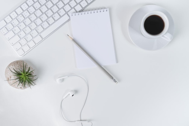 White office desk with blank notebook pencil computer keyboard and headphones and plant tillandsia Flat lay copy space