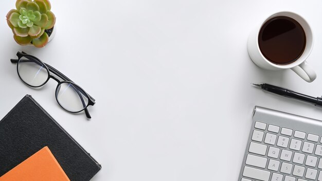 White office desk with coffee cup, glasses, notebook and cactus.