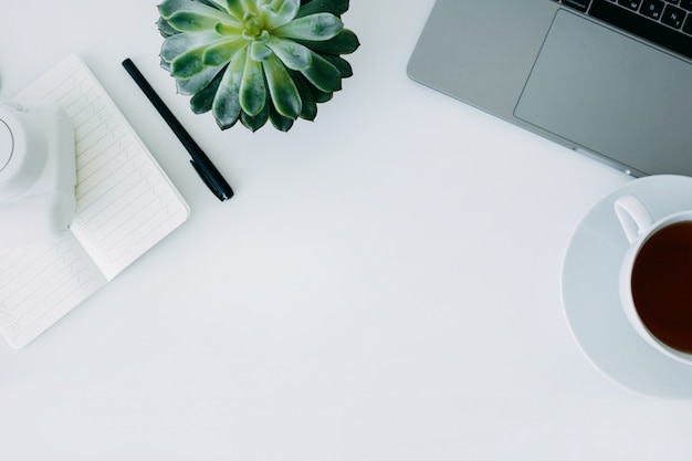 White office desk with laptop, office plant and notebook with pen, mini camera and cup of tea. Top view with copy space, flat lay