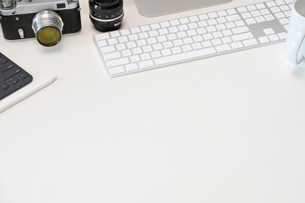 White office desk workspace table with tablet, vintage camera, lens, computer 