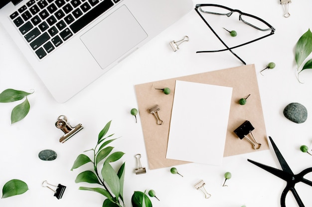 White office desk workspace with paper blank, green leaves and office supplies