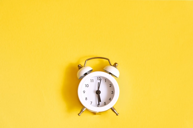 White old alarm clock on yellow. Wake up at noon. 