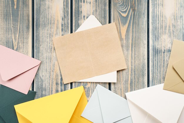 White open envelope with open kraft paper card on gray wooden background Multicolored envelopes lie by side Copy space