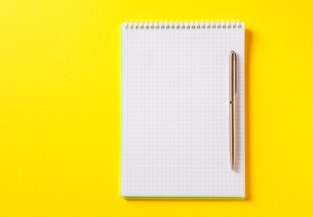 The white open notepad on silver pen isolated on yellow