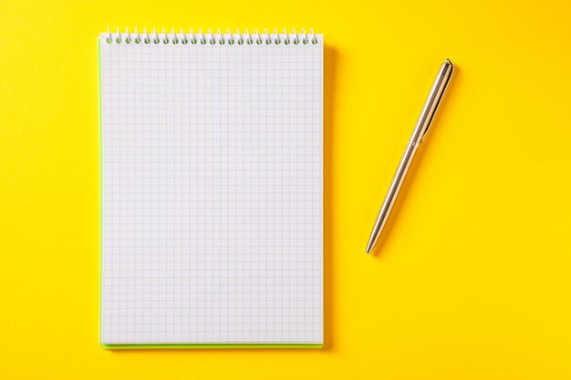 The white open notepad on silver pen isolated on yellow