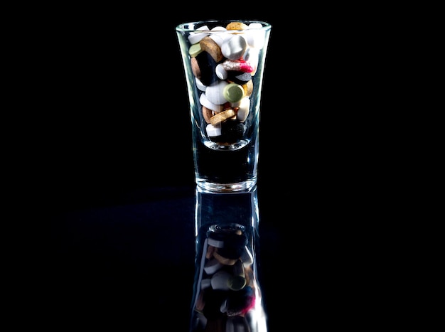 White orange pills in wineglass glass in jar in bucket Isolated on black set of capsule and pills inside closeup