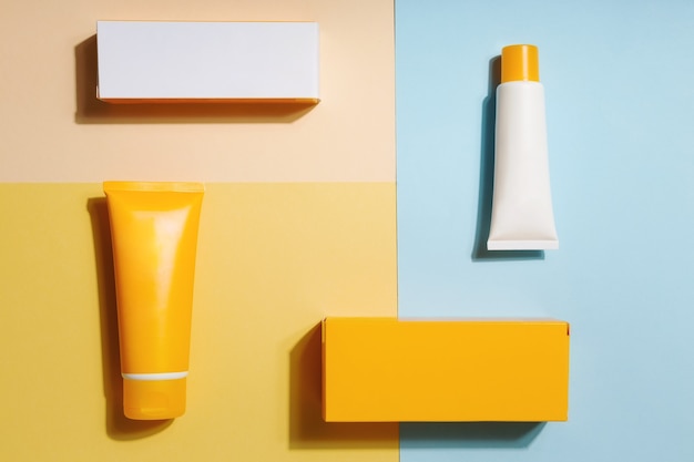 White and orange tubes and boxes of sunscreen on yellow and blue background Sun Protection