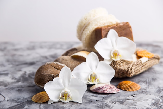 White orchid flowers next to sea stones and shells on a gray background 