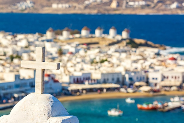 백색 정교회는 여름 화창한 날 에게 해 그리스에 붉은 교회로 유명한 풍차 선박과 요트가 있는 미코노스 섬의 코라 항구를 가로질러 교차합니다.