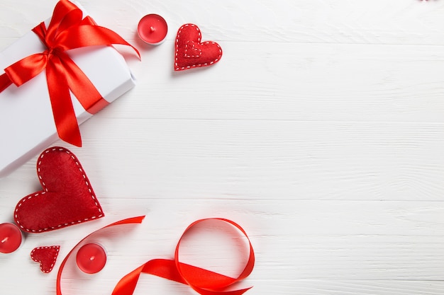 White packed gift with red ribbon, candles and handmade heart on the table. A romantic valentine's day surprise for a loved one.