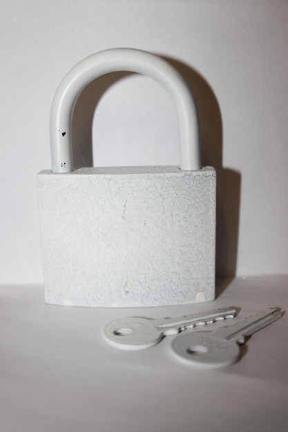 A white padlock with a key on it is attached to a wall.