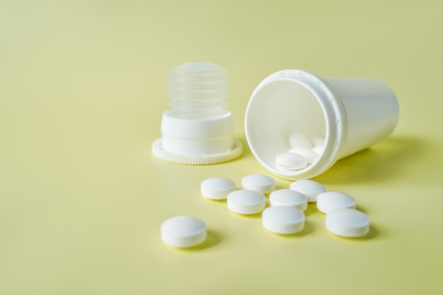 Белые обезболивающие таблетки в банке на желтом фоне концепция здравоохранения и медицины