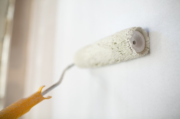 White paint roller in hand with drywall wall.