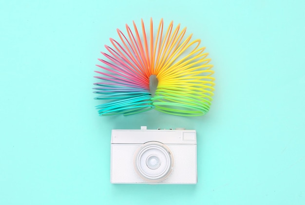 White painted camera and Rainbow plastic multicolored spiral slinky toy on blue background Imagination and inspiration