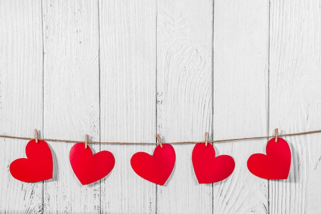 White painted wooden background with a garland of red hearts. Natural rope and clothespins. Concept of recognition of love, romantic relationships, Valentine's day in grunge style. Copy space