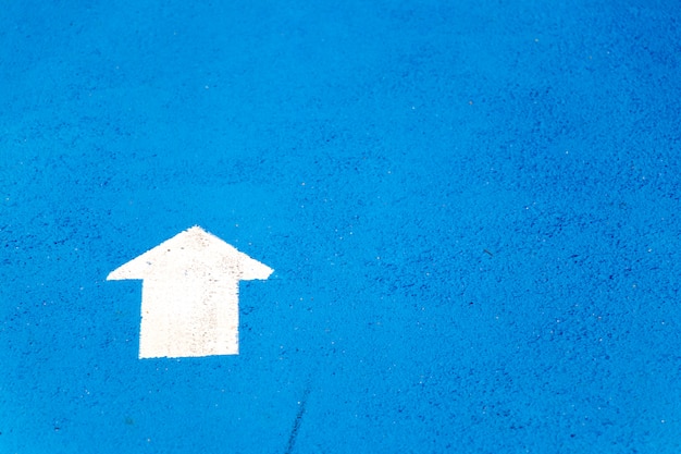 White painting in forward direction arrow symbol on blue concrete road background