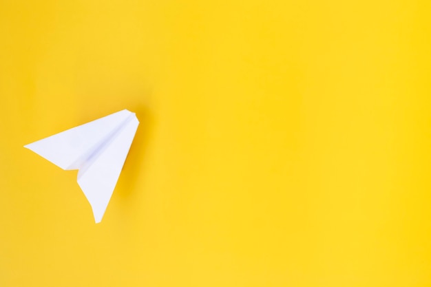 Белый бумажный самолетик на желтом фоне. Концепция