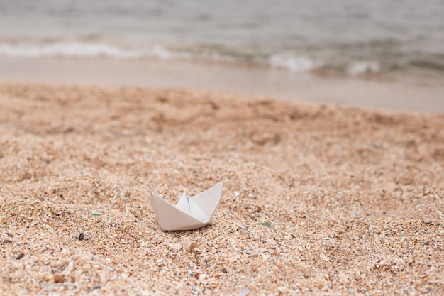 White paper boat on sand near sea on autumn or sunny day Small boat from paper on sand near sea waves Concept Travel tourism vacation rest holilday