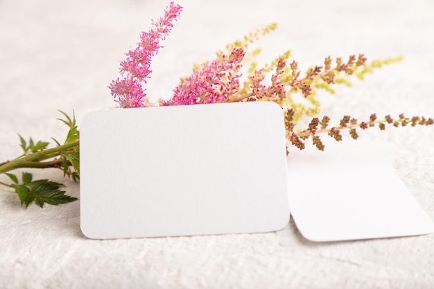 White paper business card mockup with purple astilbe flowers on\
gray concrete background side view copy space