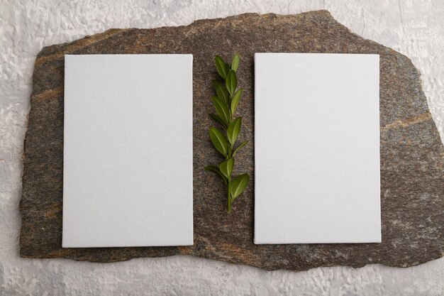 White paper business card mockup with stone and boxwood branch on gray concrete background flat lay canvas copy space